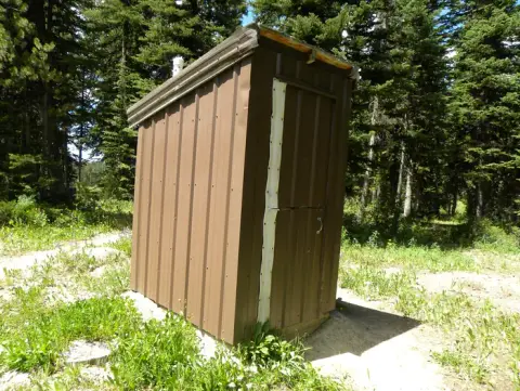 An outhouse stands in a clearing surrounded by trees.