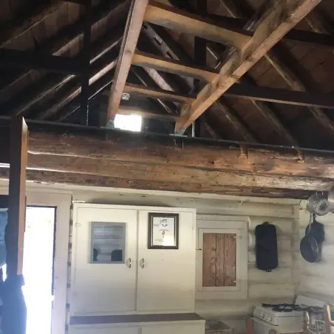 An interior view showing exposed wooden roof beams and white cabinets inside a rustic log cabin.