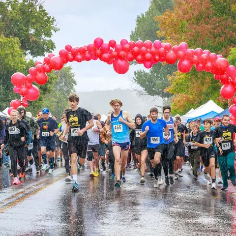 Runners participate in a race under an arch of red balloons in the rain.