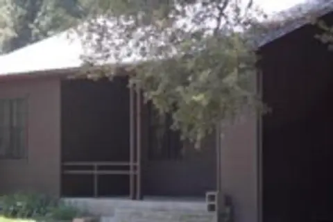 An exterior view of a building with a porch, partially obscured by a tree branch.