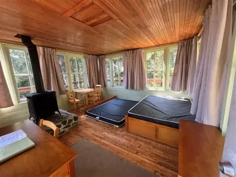 An interior view of a rustic wooden cabin featuring beds and a wood stove.
