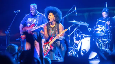 A band performs on stage with a singer playing guitar, a bassist, and a drummer.