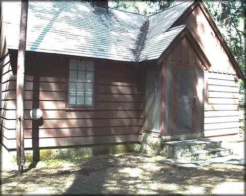 Exterior view of a dark brown cabin with a shingled roof and a screened entryway.