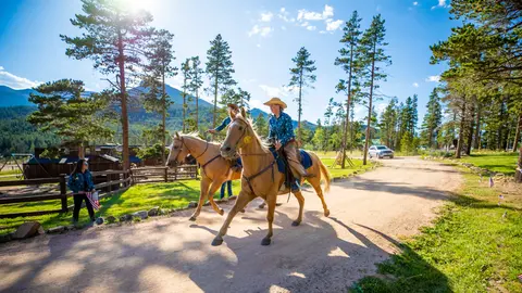 Two people ride horses along a dirt path.