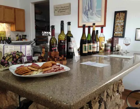 A tasting counter displays various wine bottles, crackers, meat, and cheese.