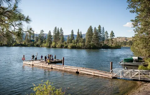 People fishing on a wooden dock extending into a lake surrounded by trees.