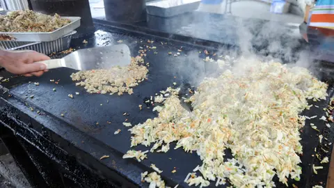 A person cooks food on a large flat top grill.