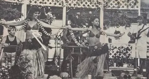 Two women performing a dance in traditional skirts accompanied by musicians.