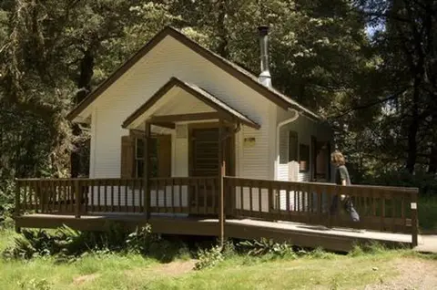 A small white building with a wooden porch and ramp surrounded by trees.