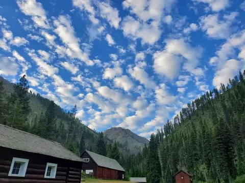 A scenic view of a mountain valley with wooden buildings and a cloudy blue sky.