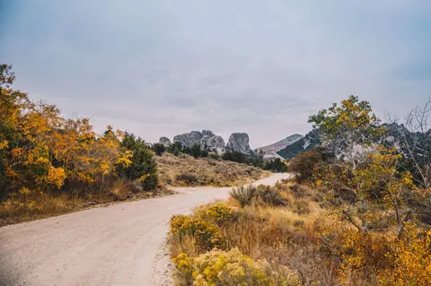 A dirt road winds through an autumn landscape with rocky outcrops under an overcast sky.