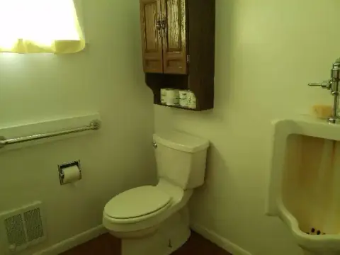 A small interior restroom with a toilet, urinal, and wall cabinet.