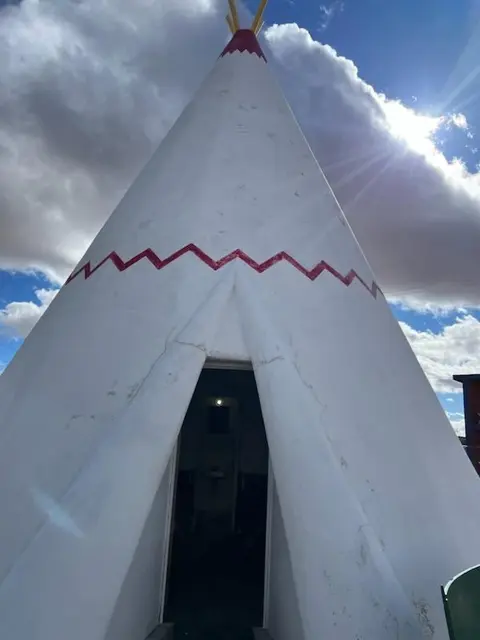 A tall white teepee-shaped structure stands outdoors under a cloudy sky.