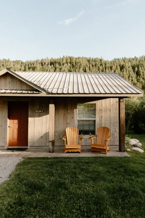 Exterior of a rustic wooden cabin with two Adirondack chairs on the porch.