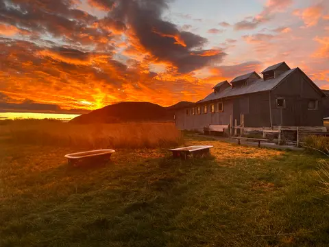 A vibrant sunset sky over a rustic building and fields with two bathtubs outside.