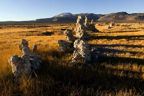 Tufa towers stand in a dry grassy landscape under a clear blue sky with mountains in the background.