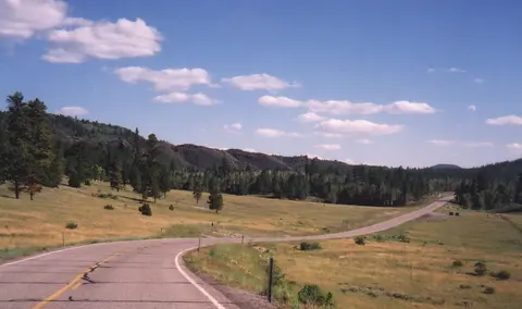A winding road runs through a grassy valley beneath a blue sky.