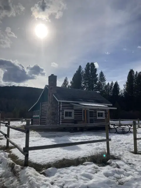 A log cabin in a snowy landscape under a bright sun.
