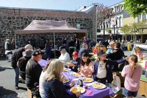 People gather at outdoor tables for a meal under a canopy.