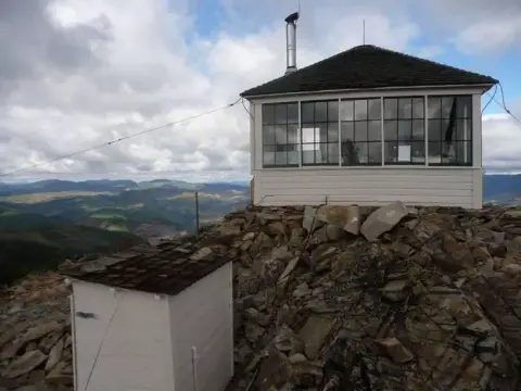 A fire lookout building stands on a rocky mountain summit.