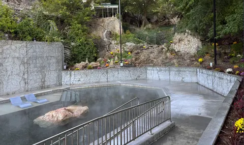 An outdoor hot spring pool surrounded by stone walls and landscaped hillside gardens.