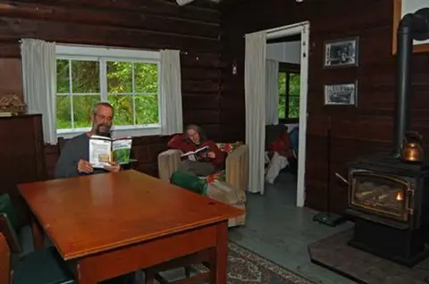 Two people reading books inside a rustic wooden cabin.