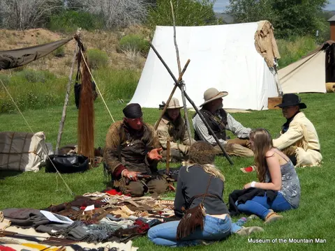 People in historical clothing sitting on grass near tents.