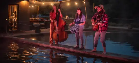 A band plays music standing by a pool at night.