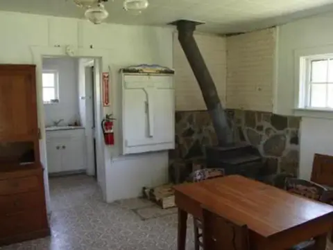 A photograph shows the interior of a room with a wood-burning stove and wooden table.