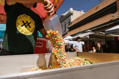A vendor scoops colorful popcorn into a bag at an outdoor event.