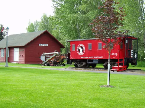 A red depot building and a red caboose parked on a lawn.