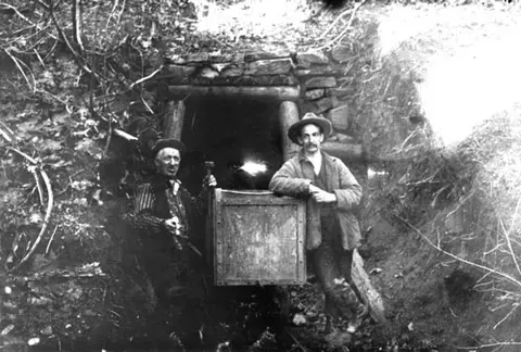 Black and white historic photograph showing two men standing in front of a mine entrance.