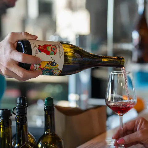 A person pouring wine from a bottle into a glass indoors.
