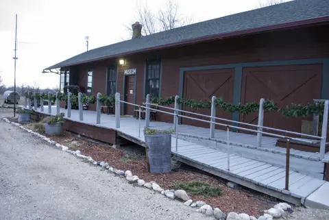 Exterior view of a historic museum building with a wooden porch and ramp decorated with holiday garlands.