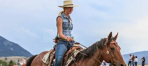 A woman wearing a hat and riding a horse outdoors.