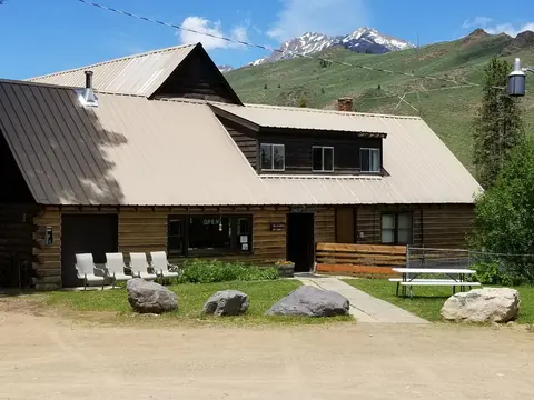 A rustic wooden building with a metal roof stands in front of a green mountain range.