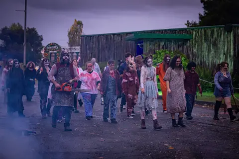 A group of people dressed in horror and zombie costumes walk along an outdoor path.