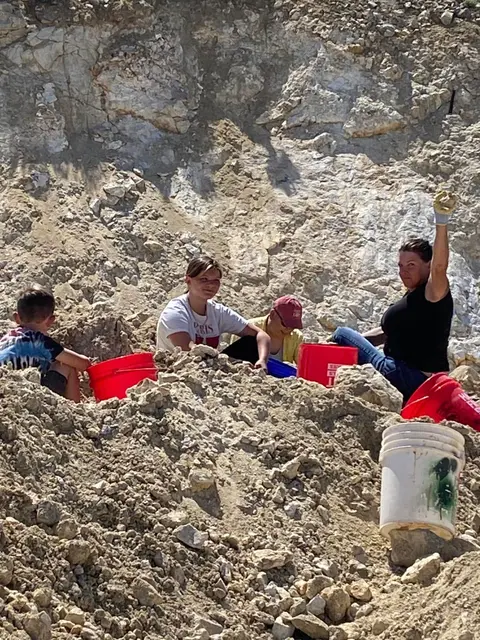 People digging in a rocky dirt area with buckets.