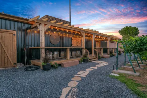 An exterior view of a winery building with a wooden pergola under a sunset sky.