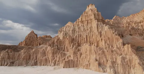 A dramatic landscape of eroded rock formations under a dark, cloudy sky.