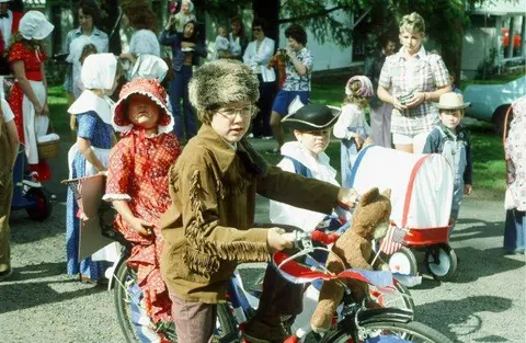 Children dressed in historical costumes ride decorated bicycles and wagons in an outdoor parade.