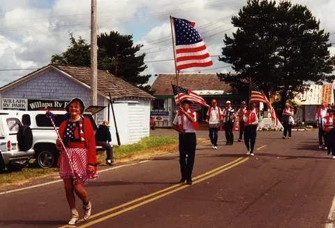 People walking in a parade holding American flags along a street.