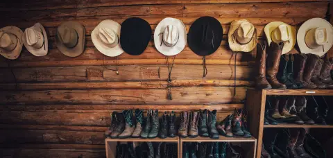 Cowboy hats and boots are displayed against a rustic log wall.