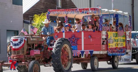 A decorated tractor pulling a trailer full of people in a parade.