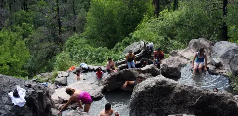 People enjoy soaking in natural rock pools surrounded by lush green trees.