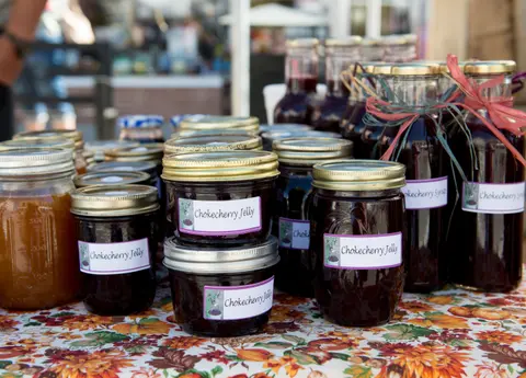 A display of jars and bottles of chokecherry jelly and syrup on a table.