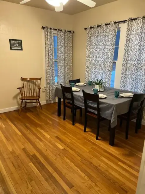 A dining room with a table set for meals, wooden floors, and patterned curtains.
