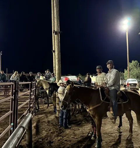 People on horseback gathered at night by an arena.