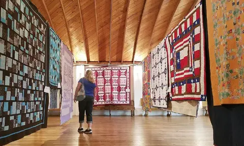 A visitor looks at quilts displayed inside a wooden building.