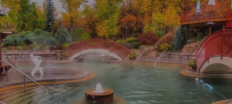 An outdoor hot spring pool surrounded by autumn trees and red bridges.